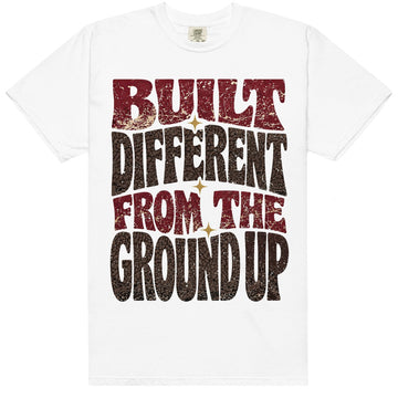 White HeatLit ‘Built Different From The Ground Up’ tee with a Bin 23 front graphic — cardinal-red type, chocolate-brown elephant print and gold star sparks on a cream speckle.
